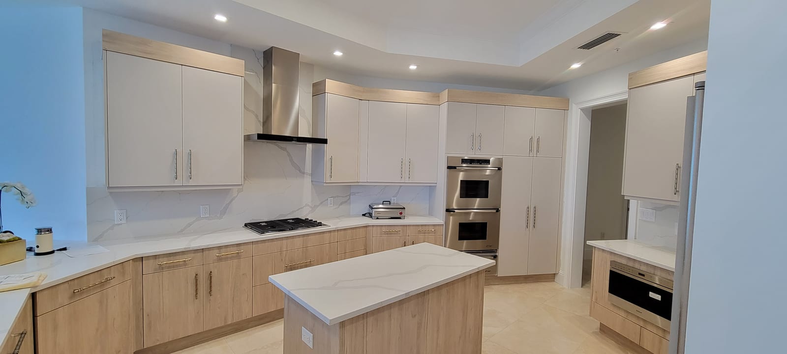 Modern white kitchen with custom cabinetry, marble island, and double oven